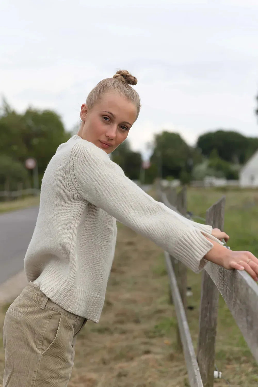 Strickpullover aus 100% Wolle mit Knopfdetails, getragen in natürlicher Umgebung, betont den Wohlfühlkomfort und die Atmungsaktivität.