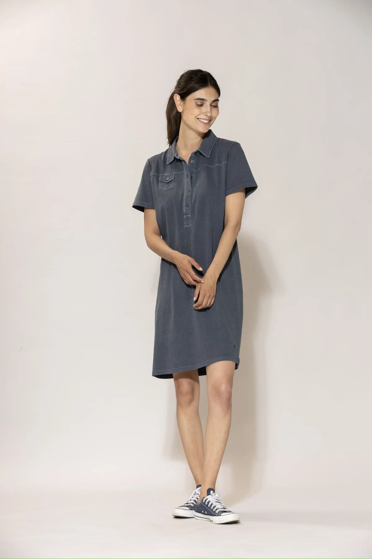 Frau trägt das Louise Polo Kleid in Dusty Navy, Frontansicht, kombiniert mit dunklen Sneakers #farbe_dusty navy