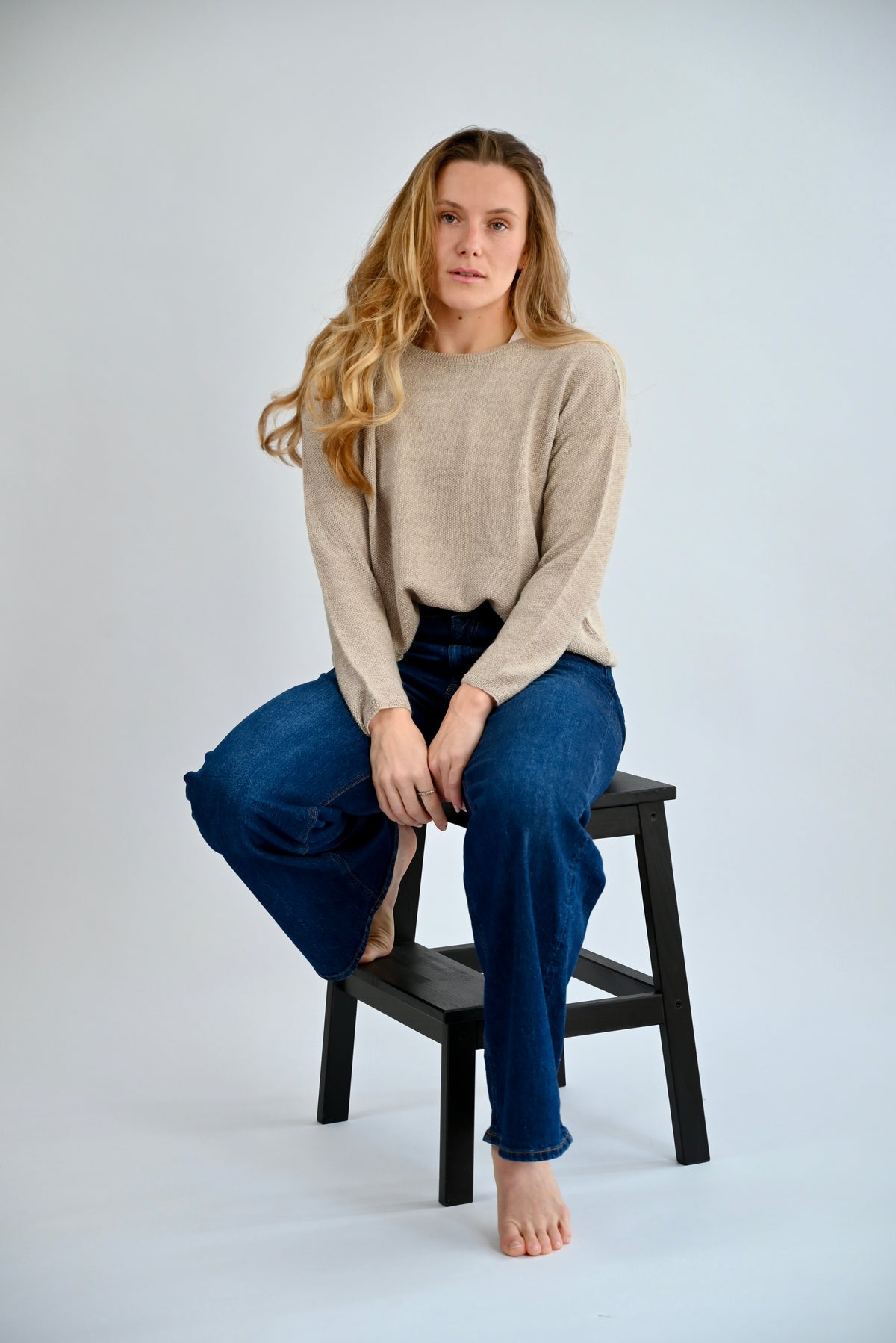 DANA Raglan Sweater in Light Grey, sitzende Frontansicht am Model auf Hocker, anliegender Reisstich und weicher Fall