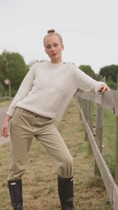 Beiger Wollpullover mit Knopfdetails an der Schulter, kombiniert mit Cordhose und Gummistiefeln, perfekt für kühle Outdoor-Tage.