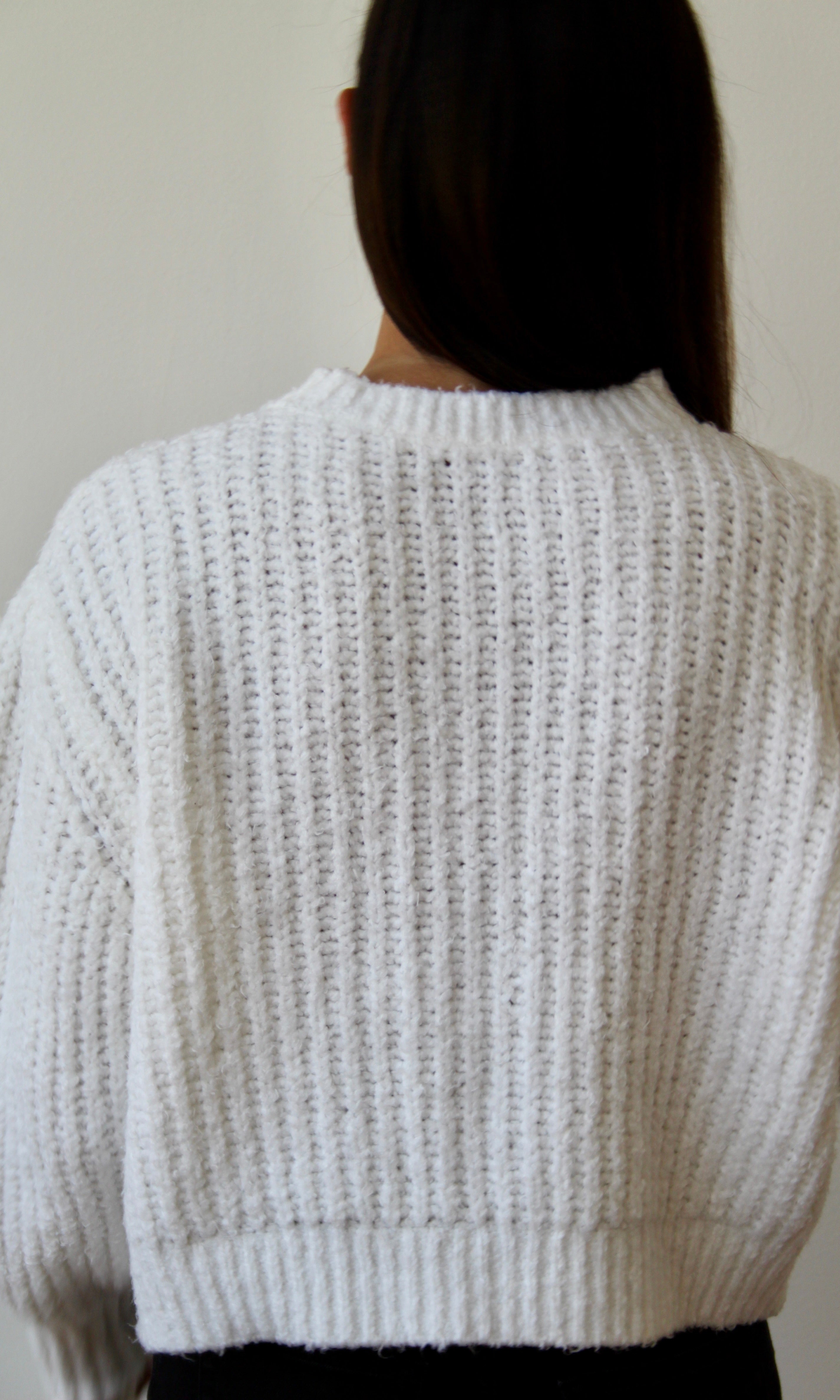 Frau mit weißem, grob gestricktem Baumwollpullover von hinten